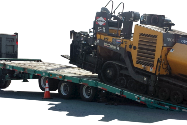 Asphalt paver being loaded onto a Felling Trailers deck-over trailer with air ramps, showing low load angle for paving equipment transport.
