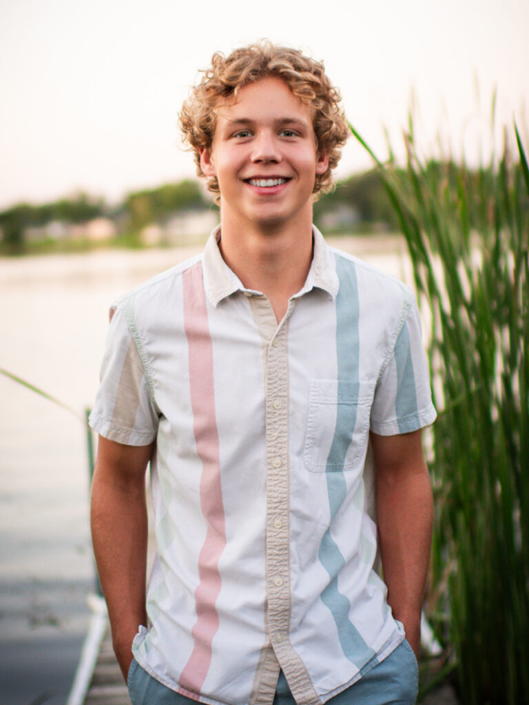 2026 Sauk Centre graduate and Felling Trailers team member Keegan Christians standing on a dock near lakeside reeds.