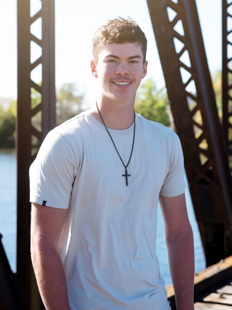 2026 Long Prairie-Grey Eagle graduate Travis Warner standing outdoors on a bridge near the water.