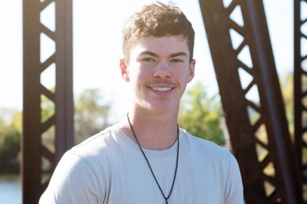2026 Long Prairie-Grey Eagle graduate Travis Warner standing outdoors on a bridge near the water.
